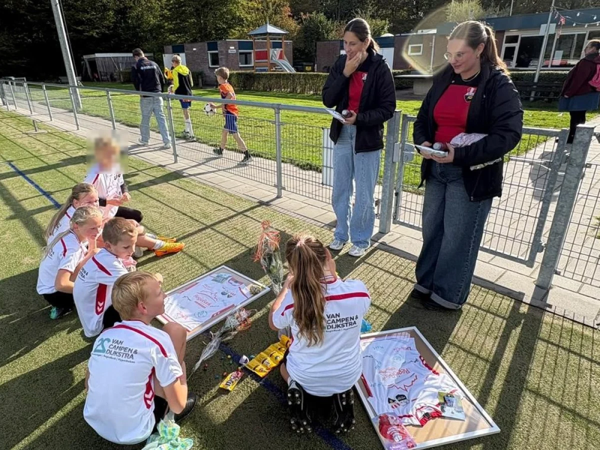 De spelers van de J2 zitten op het veld bij hun ingelijste wedstrijdshirts